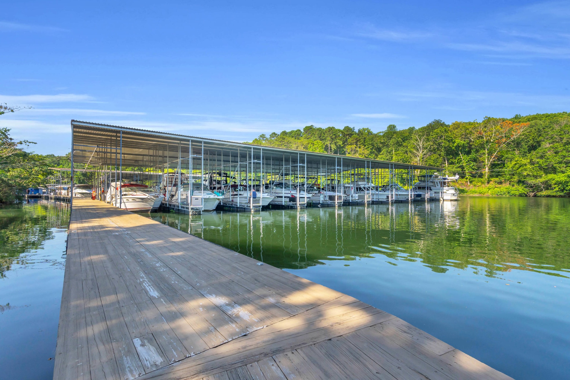 Wooden main dock at Shady Grove Harbor leading past a long row of covered boat slips filled with cruisers and yachts.